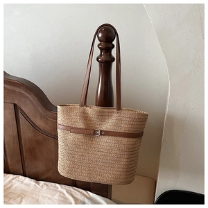 Detail of woven straw tote bag featuring brown leather handles and a silver metal buckle