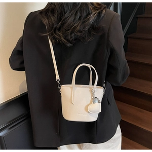 Detail of a creamy white bucket bag with pebble leather texture and heart charm