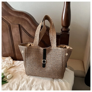 Détail du sac cabas en paille tressée avec sangle en cuir noir et boucle sur lit blanc