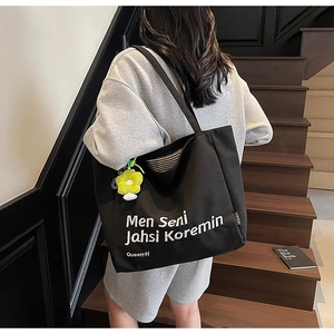 Detail of a black canvas tote with white artistic lettering and a yellow flower charm