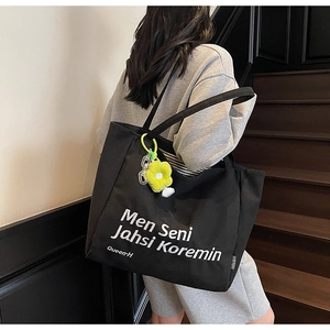 Close-up of large black canvas tote bag with white text and yellow flower pendant detail