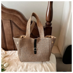 Détail du sac cabas en paille tissée avec sangle en cuir noir et finitions métalliques dorées