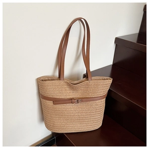 Detail of woven straw tote bag featuring brown leather handles and decorative buckle