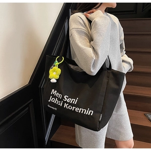 Detail of a large black canvas tote bag with white lettering and a yellow flower charm