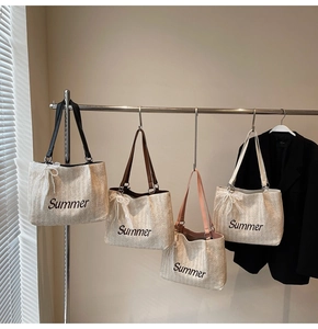 Detail of straw tote bags with Summer embroidery and colorful straps in four colors