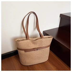 Close-up of woven straw tote bag with brown leather straps and silver metal buckle detail