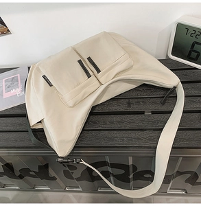 Detail of beige nylon crescent bag featuring double front pockets and plastic buckle strap