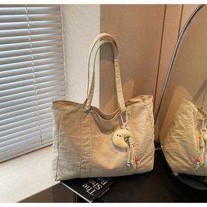 Detail of beige nylon tote bag with green embroidery and yellow moon plush pendant