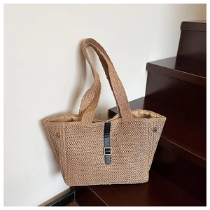 Détail d'un sac cabas en paille avec lanière en cuir noir et boucle sur un escalier bois