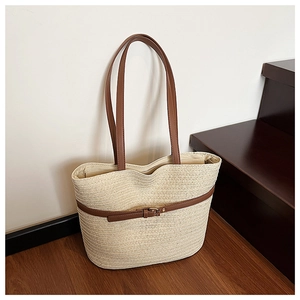 Detail of cream woven straw tote bag with brown leather handles and buckle strap