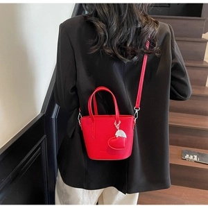 Detailed view of red bucket bag with heart charm and shoulder strap on model