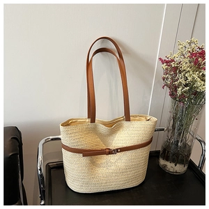 Detailed close-up of the straw woven tote bag featuring a brown synthetic leather strap