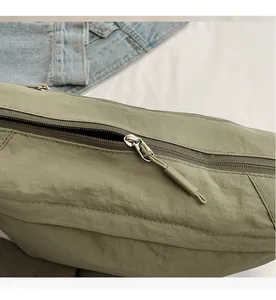 Detail view of smooth silver zipper and textured green nylon fabric on crossbody bag