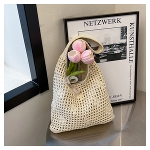 Close-up of cream hollow woven bucket bag with pink tulips inside on a metal table