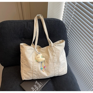 Detail of beige canvas tote bag with moon plush charm on a blue corduroy sofa