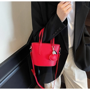 Detail of red pebbled leather bucket bag with heart charm and detachable shoulder strap