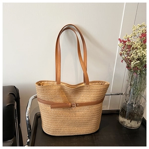 Detail of hand-woven straw tote with brown leather strap and golden metal buckle finish