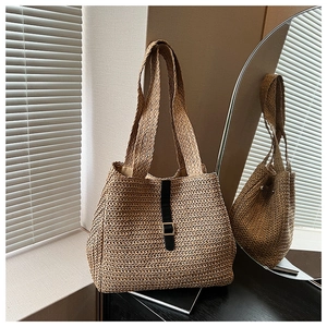 Détail de la texture d'un sac cabas en paille avec lanière en cuir noir et boucle dorée