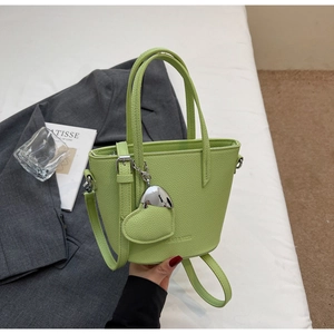 Detail of light green bucket bag with lychee texture and heart charm on fabric