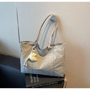 Detail of grey-green nylon tote bag with brand embroidery and yellow moon plush charm