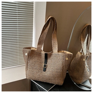 Détail d'un cabas en paille tissée avec sangle en cuir noir et boucle dorée chic