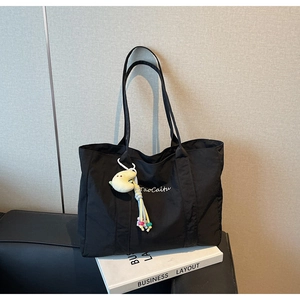 Detail of black canvas tote bag featuring white embroidery and a plush moon charm accessory