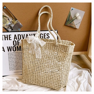Dettaglio borsa tote in paglia intrecciata con trama a rete e fiocco in pizzo bianco