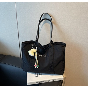 Detail of black tote bag with white TaoCaitu embroidery and plush moon charm accessory