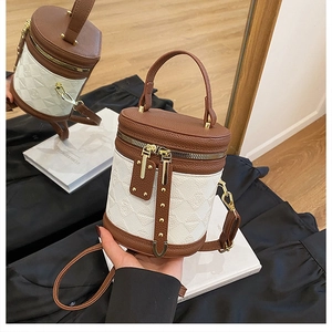 Detail of cylinder bucket bag featuring brown leather, white embossed fabric and gold hardware