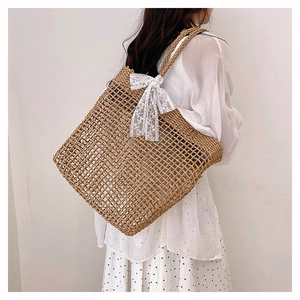 Dettaglio della borsa tote in paglia intrecciata con un delicato fiocco di pizzo bianco