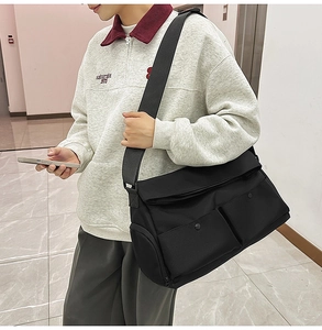 Détail du sac messager en toile noire avec deux poches avant et bandoulière réglable