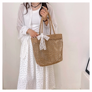 Dettaglio della borsa tote in paglia intrecciata con fiocco in pizzo bianco e trama