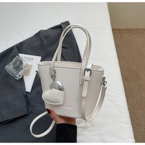 Close-up of white lychee grain leather bucket bag featuring heart charm and brand logo
