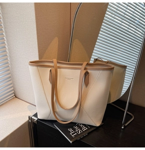 Detail of off-white lychee grain leather tote bag with contrast piping on wooden surface