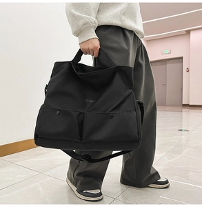 Détail du grand sac cabas noir avec deux poches avant à bouton-pression et bandoulière