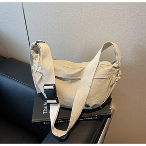 Detail of beige nylon crescent crossbody bag featuring wide fabric strap and plastic buckle