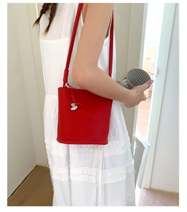 Détail du sac seau en cuir grainé rouge avec pendentif cœur sur une robe blanche