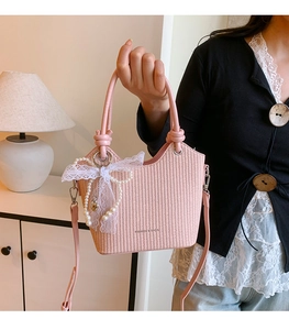 Détail du sac seau rose tressé avec pendentif en perles et lettrage fashion élégant