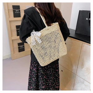 Dettaglio della borsa in paglia beige con fiocco in pizzo bianco e trama intrecciata