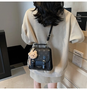 Mini-Rucksack aus schwarzem Leder mit Elch-Motiv und Teddy-Anhänger auf beigem Pullover