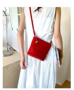 Sac seau rouge en cuir grainé porté sur une robe blanche pour un contraste de couleurs chic