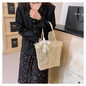 Dettaglio della borsa tote in paglia intrecciata con fiocco di pizzo bianco e manici robusti