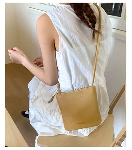 Sac seau en cuir jaune moutarde porté avec une robe blanche dans un décor minimaliste