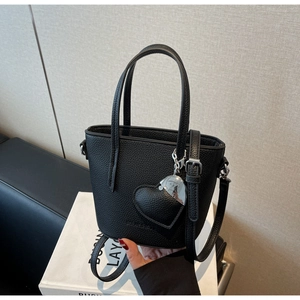 Detail of black pebbled leather bucket bag featuring a heart charm and adjustable strap