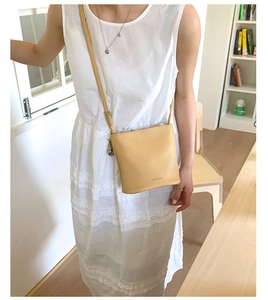 Détail d'un sac seau en cuir litchi jaune crème avec logo de la marque et bandoulière