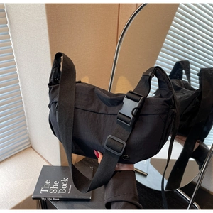 Detail of black nylon crossbody bag featuring wide woven strap and large plastic buckle