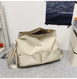 Détail du grand sac messager en toile beige avec deux poches à bouton-pression
