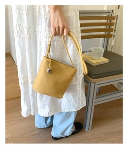 Gros plan du sac seau jaune en cuir avec breloque argentée et logo Pantor embossé