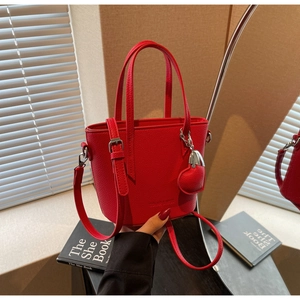 Close-up of a red bucket bag with litchi texture and a decorative heart pendant