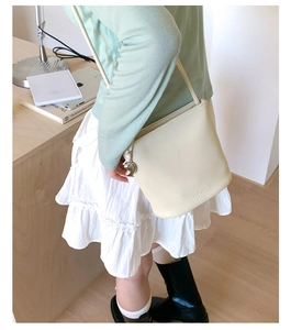 Détail d'un sac bandoulière beige en cuir grainé avec breloque cœur argentée et logo